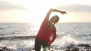 Kadınlar gün batımında deniz kıyısında egzersiz yapmadan önce esneme hareketleri yaparlar.