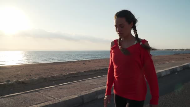Junges motiviertes Mädchen bereitet sich darauf vor, bei Sonnenuntergang am Strand zu laufen — Stockvideo