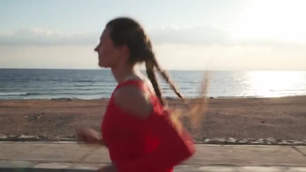 Jovem garota motivada correndo no calçadão ao pôr do sol perto do oceano — Vídeo de Stock