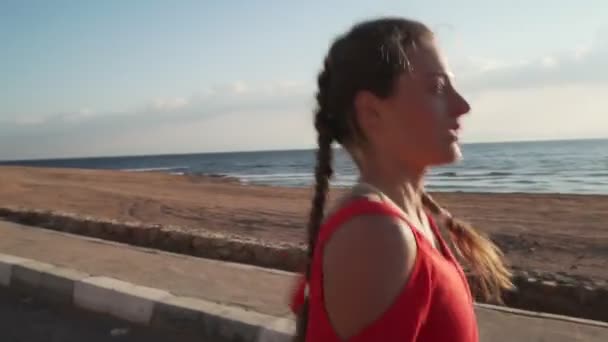 Young caucasian girl running on promenade at sunset near ocean — Stockvideo