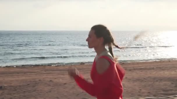Όμορφη γυναίκα που κάνει τζόκινγκ σε μια βόλτα στο ηλιοβασίλεμα κοντά στον ωκεανό — Αρχείο Βίντεο