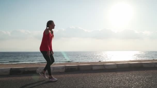 Mujer joven y deportiva trotando en la playa y se detiene para recuperar el aliento — Vídeo de stock