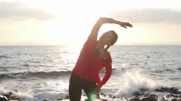 Mujer hacer estiramiento antes del entrenamiento en la orilla del mar al atardecer — Vídeos de Stock