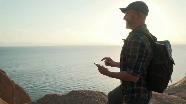 Yakışıklı yaşlı gezgin, gün doğumunda el kamerasında akıllı telefon kullanıyor.