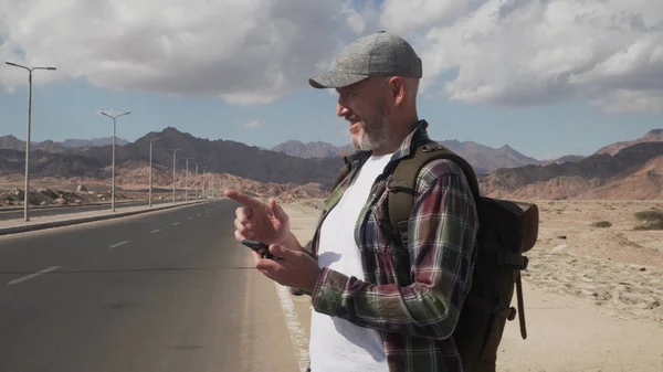 Son sınıf erkek gezgin, tek başına bir yolda duran cep telefonu kullanıyor.
