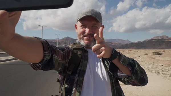 Son sınıf öğrencisi erkek, akıllı telefonuyla çölde yol kenarında selfie çekiyor.