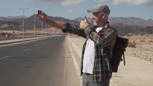 Son sınıf öğrencisi erkek, akıllı telefonuyla çölde yol kenarında selfie çekiyor.