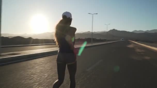 Joven chica motivada trotando en la carretera al atardecer — Vídeo de stock