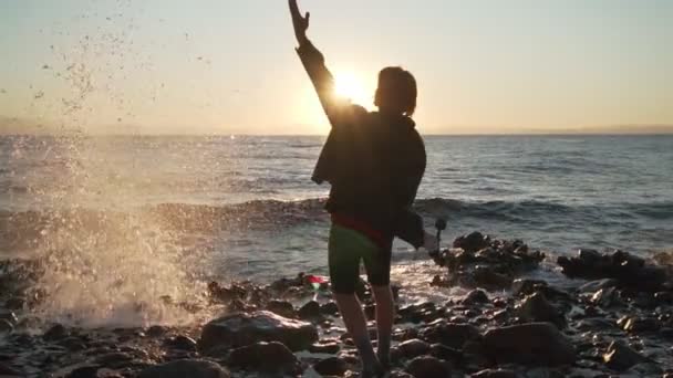 若いです男の子ホップオン場所で彼のスケートボードとともに日没の海岸で急速なスローモーション — ストック動画