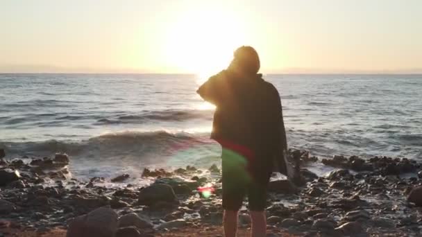 Мальчик со скейтбордом прогуливается по берегу моря на съемках заката — стоковое видео