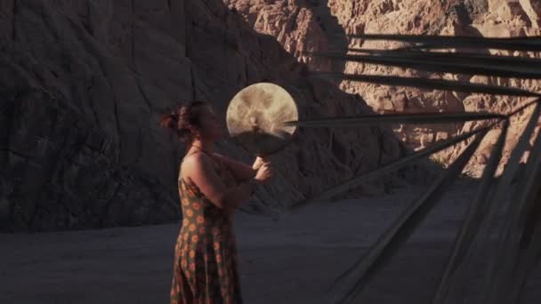 Ung kaukasisk kvinna spelar tamburin i bergen skugga i öknen vid solnedgången — Stockvideo