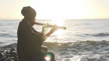 Bansuri çalgıcısı enstrümanını deniz hokeyinde gün batımında çalıyor.