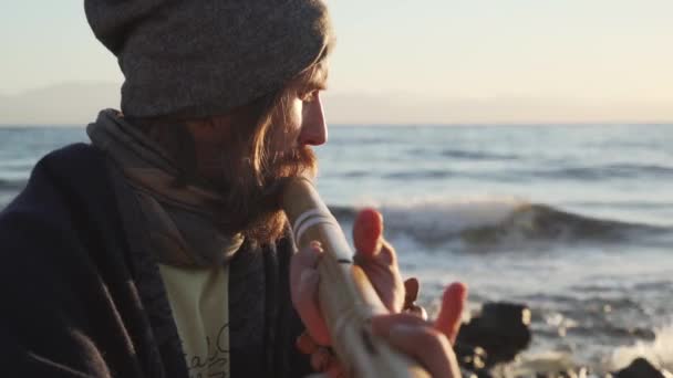 Close up man playing on bansuri traditional Indian instrument at sunrise seaside — Stock Video