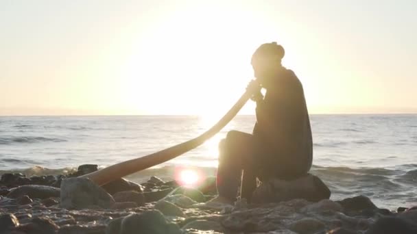 Hombre tocando didgeridoo instrumento de viento australiano en el sol en la orilla del mar — Vídeo de stock