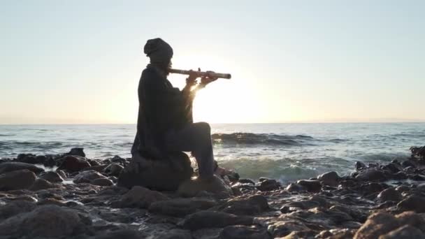 Man playing on Indian Bansuri instrument in sunshine at sea shore — Stock Video