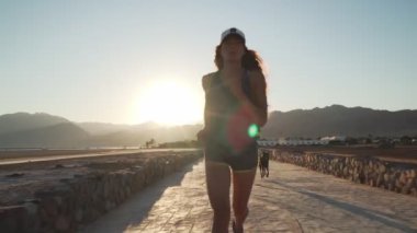 Güzel beyaz kız gün doğumunda çöl kaldırım yolunda köpeğiyle koşuyor.