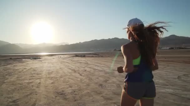 Achteraanzicht van fit meisje joggen in droge woestijn bij zonsopgang snelle slow motion — Stockvideo