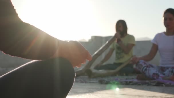 Lidé praktikují meditaci, zatímco mladý muž hraje didgeridoo na slunci — Stock video