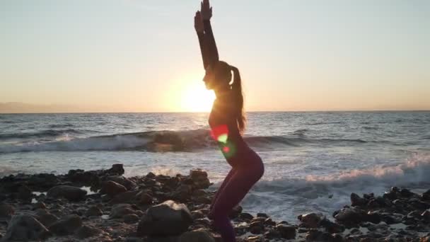 Fille caucasienne flexible faisant chaise yoga asana au bord de la mer au coucher du soleil — Video