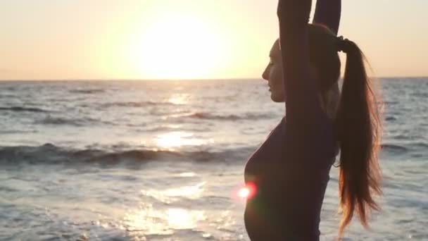 Side view of young caucasian girl practicing yoga at sunset seashore — Stock Video