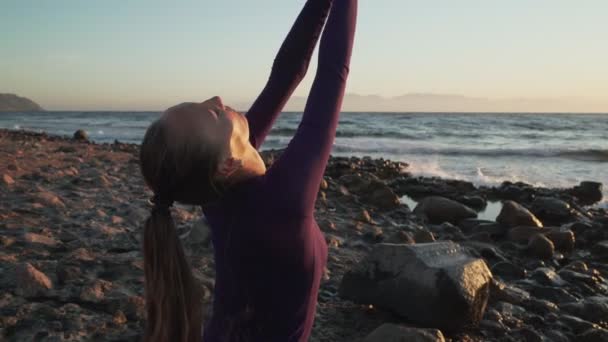 Junge Frau sitzt in Namaste-Pose und meditiert bei Sonnenuntergang am Meer — Stockvideo