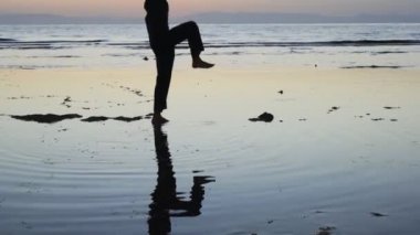 Gün batımında deniz kenarında Çigong 'un elementlerini pratik yapan bir adamın silueti.