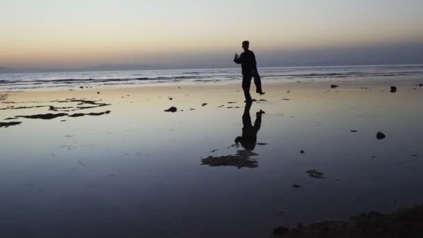 Silhouette man practice qigong stand at mirrored surface of sunset shallow water — Stock Video