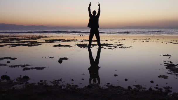 Mann praktiziert Qigong-Übungen, flaches Wasser spiegelt Figur wider — Stockvideo