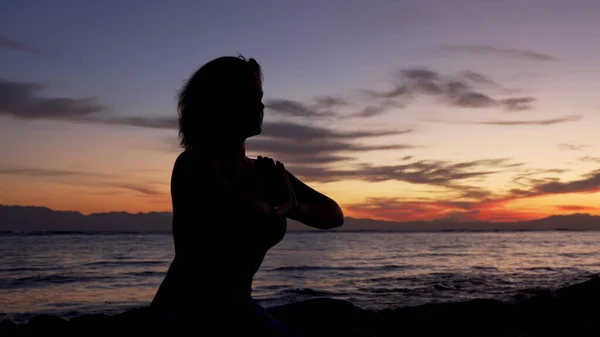 Silueta de chica se sienta en namaste pose meditando junto al mar al atardecer . —  Fotos de Stock