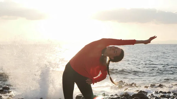 Mujer hacer estiramiento antes del entrenamiento en la orilla del mar al atardecer —  Fotos de Stock