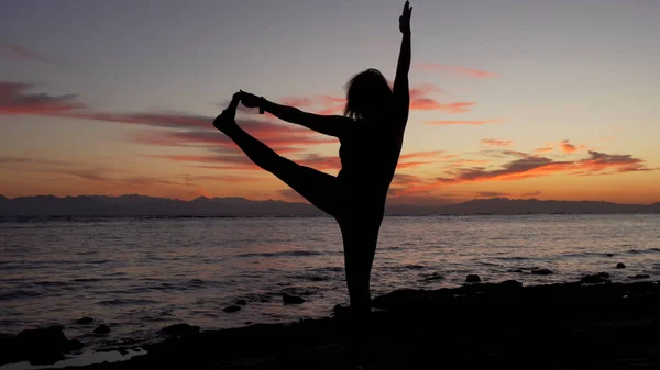Silueta de mujer haciendo yoga extendida de la mano a los pies grandes pose en el atardecer del mar . —  Fotos de Stock