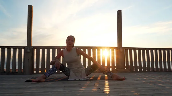 Joven chica caucásica estirando las piernas haciendo cordel en la azotea al atardecer . —  Fotos de Stock