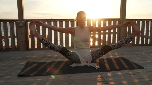 Joven chica caucásica estirando las piernas haciendo cordel en la azotea al atardecer . —  Fotos de Stock