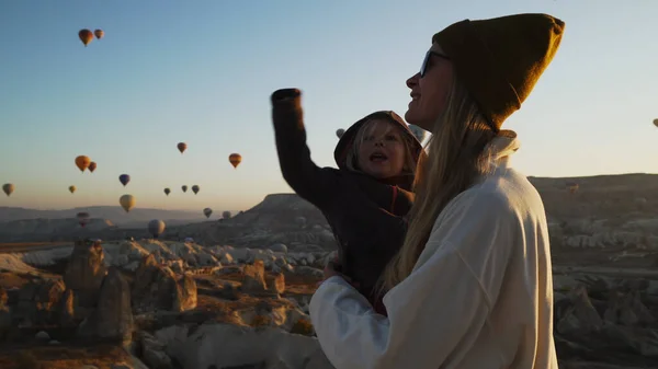 Genç sarışın anne ve çocuğu hava balonlarının önünde dönüyorlar.