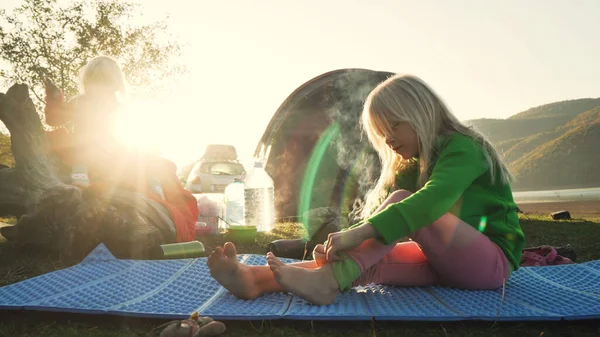 İki küçük sarışın kız kardeş kamp ateşi ve çadırın yanında oynuyorlar.