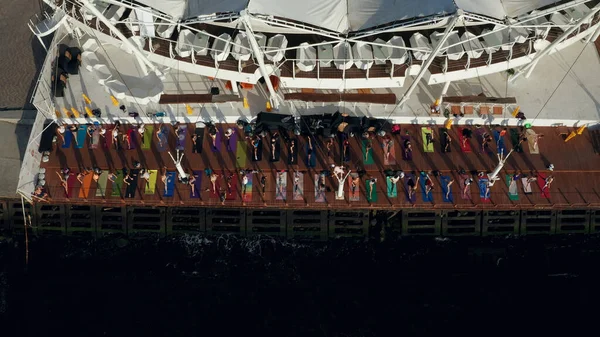 Üst tabaka insanlar deniz kıyısında renkli minderlerde yoga yapıyor.