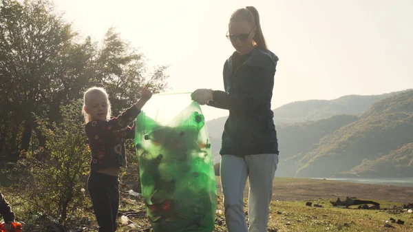 Young mother and her daughters carry a green bag full of trash counter light