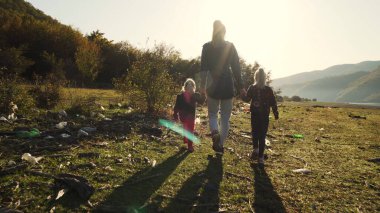 Ecological issue: mother walking with her daughters on land full of garbage