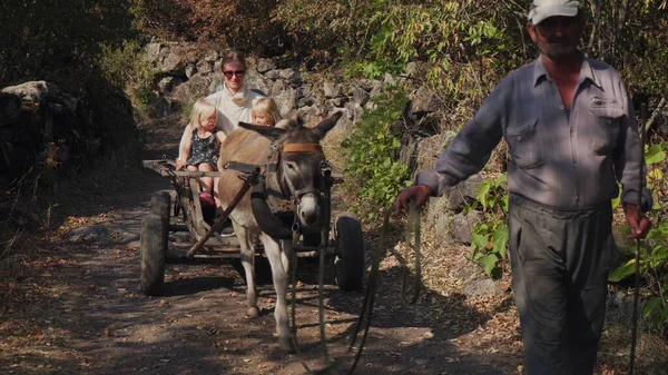 young mother with daughters ride on a donkey-drawn cart driven by grandfather
