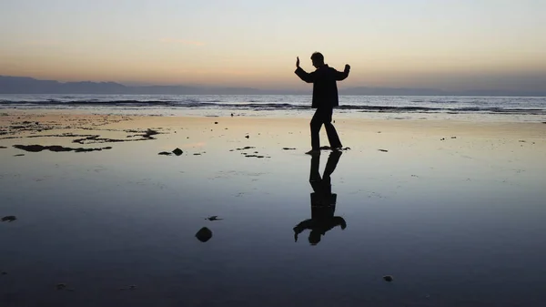 Silueta del hombre practicando ejercicios de qigong al atardecer junto al mar —  Fotos de Stock