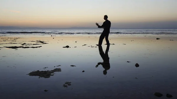 Gün batımında deniz kenarında qigong egzersizi yapan bir adamın silueti.