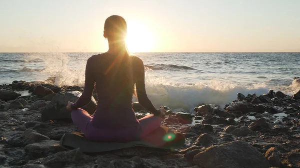 Vista trasera de la meditación de práctica femenina en el lado del mar al atardecer . —  Fotos de Stock