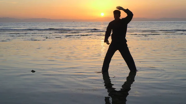 Silueta del hombre practicando ejercicios de energía al atardecer junto al mar —  Fotos de Stock