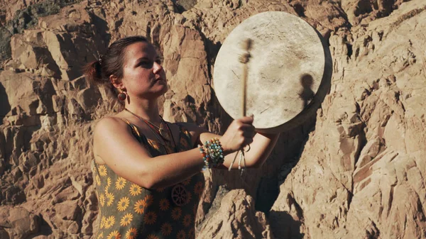 Genç beyaz bir kadın arka planda dağlarla tef çalıyor..