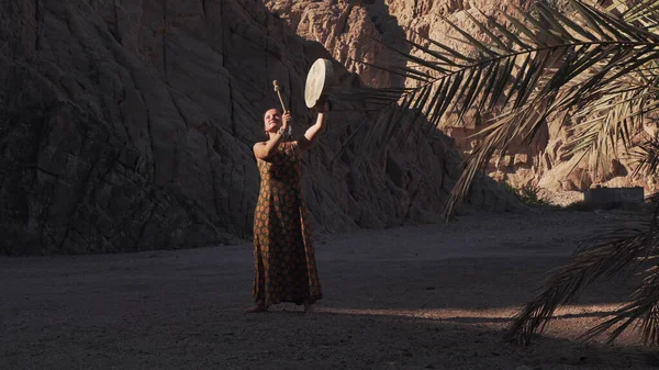 Genç kadın gün batımında çölün gölgesinde tef çalıyor. .