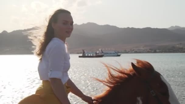 Портрет блондинки, катающейся на лошади по воде на закате замедленной съемки — стоковое видео