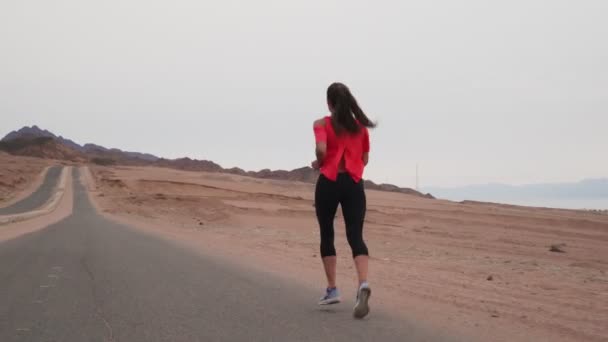Брюнетка кавказка бегает по пустынному шоссе на берегу моря — стоковое видео