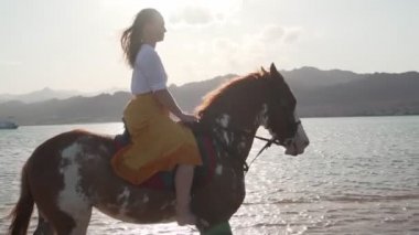 Kafkasyalı sarışın kız gün batımında ağır çekimde ata biniyor.