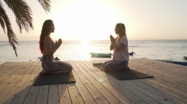 Gün batımında deniz kenarında meditasyon yapan iki kadının silueti.
