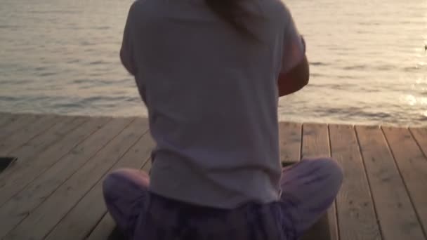 Vista trasera de las mujeres practicando yoga a la orilla del mar al atardecer — Vídeos de Stock